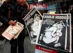 A man takes a copy of the latest edition of French weekly magazine Charlie Hebdo with the headline "One year on: the assassin is still out there," displayed Dec. 6 at a kiosk in Nice, France. Marking the one-year anniversary of when two Islamic extremists raided the magazine's offices and killed 12 people, the magazine featured a drawing of an angry God running with blood spattered on him and a machine gun slung over his back.(CNS photo/Eric Gaillard, Reuters) See VATICAN-NEWSPAPER-HEBDO Jan. 6, 2016.